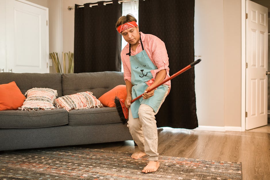 Man humorously dances with a broom while cleaning his living room.
