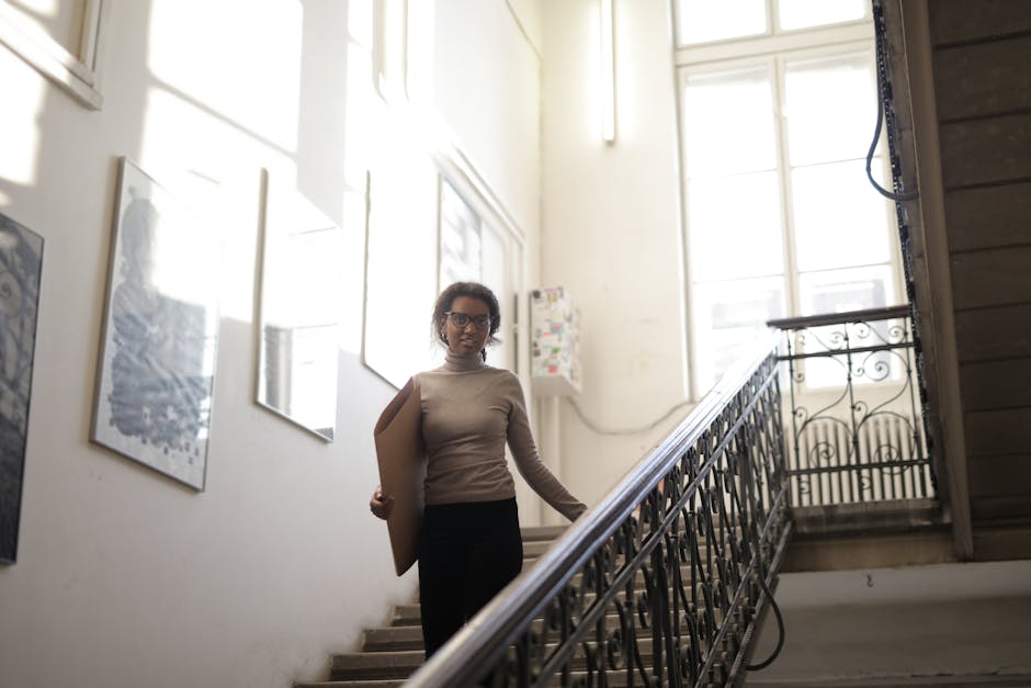A woman with eyeglasses holding a cardboard piece on an indoor staircase.